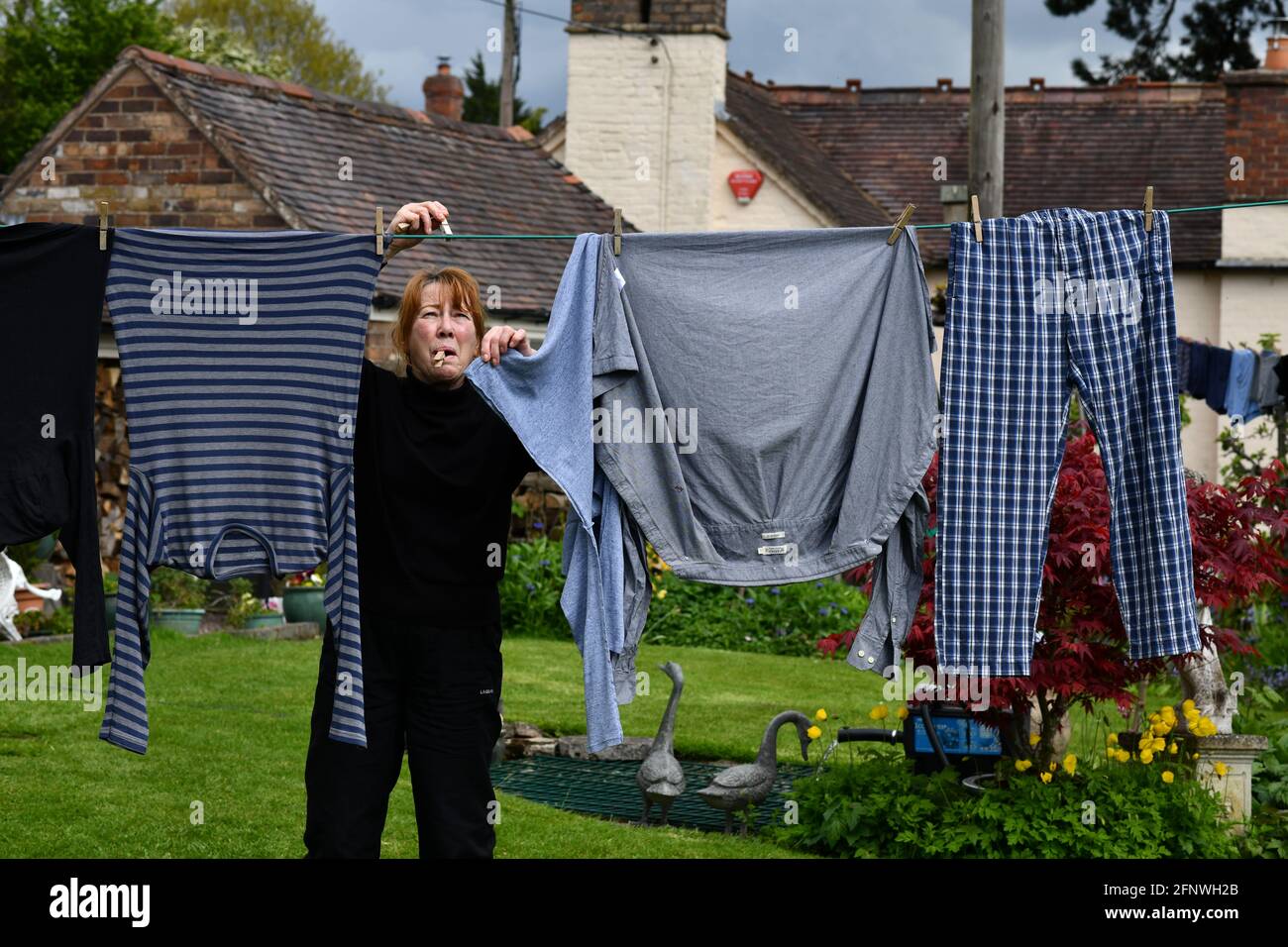 Donna appeso lavaggio su linea di vestiti con i pioli nel giardino Gran Bretagna, UK. Che asciuga fuori casa chores lavoro donne donne donna donna madre moglie Foto Stock