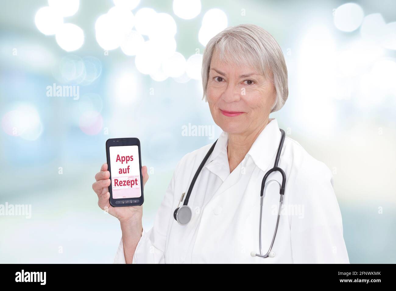 Sorridente medico senior con uno smartphone che mostra il testo tedesco Apps auf Rezept. Traduzione: App su prescrizione. Foto Stock