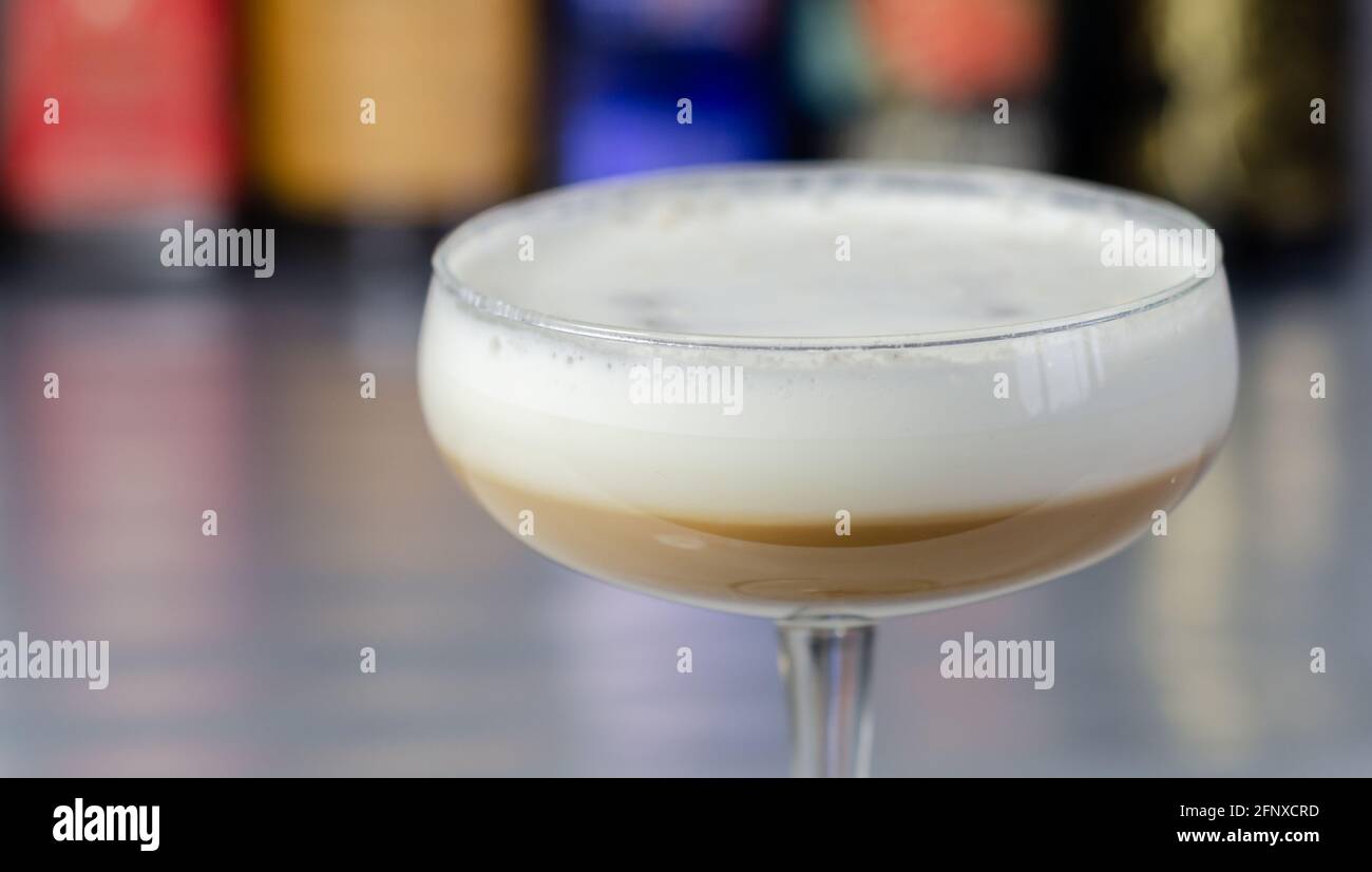 Cocktail di caffè alcolico con nota di noci e schiuma di latte soffice sullo sfondo delle bottiglie al bar, bevanda cremosa e dolce Foto Stock