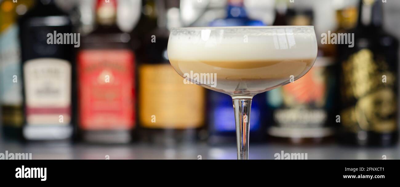 Cocktail di caffè alcolico con nota di noci e schiuma di latte soffice sullo sfondo delle bottiglie al bar, bevanda cremosa e dolce Foto Stock