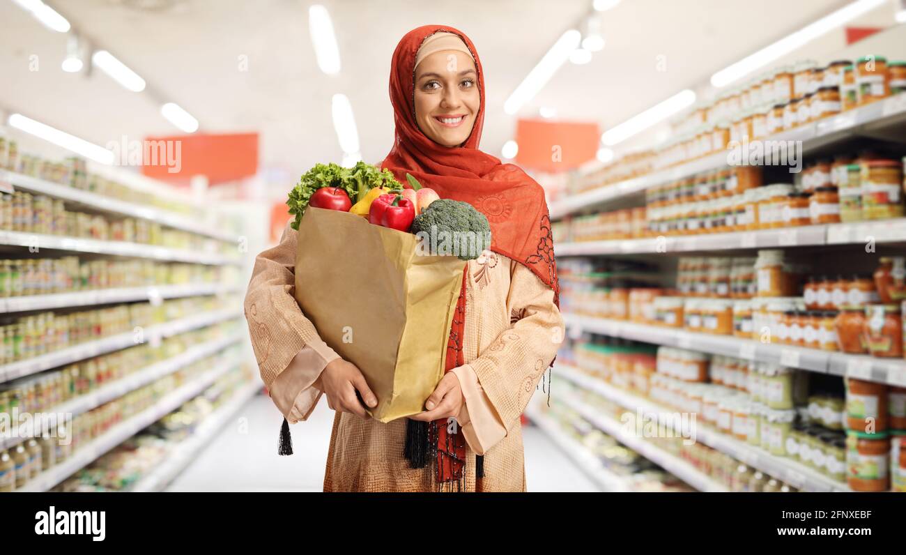 Giovane donna musulmana in abiti tradizionali che tiene un cestino della spesa in un supermercato Foto Stock