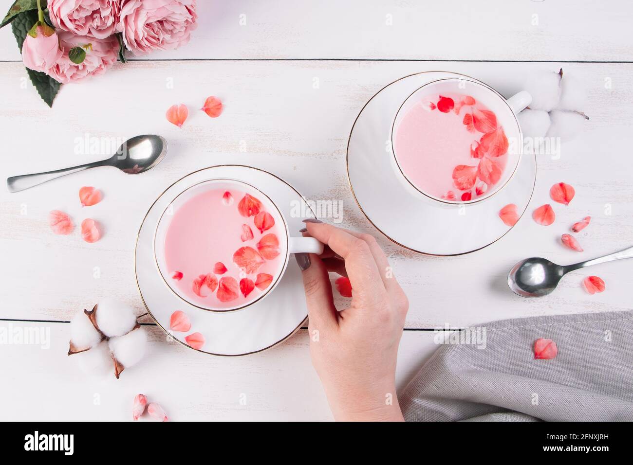 Matcha rosa con petali di rosa su sfondo bianco. La mano femminile tiene una tazza con il tè vegan di tendenza. Drink rilassante nel periodo sonnolento. Foto Stock