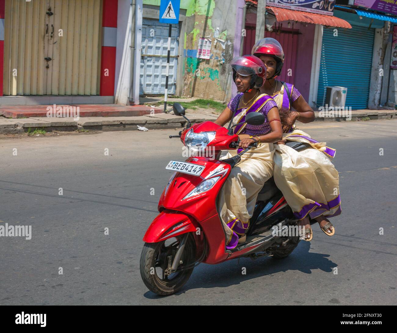 Due attraenti giri in Sri Lanka su scooter con sari dello stesso colore, con una sella laterale, Jaffna, Provincia del Nord, Sri Lanka Foto Stock