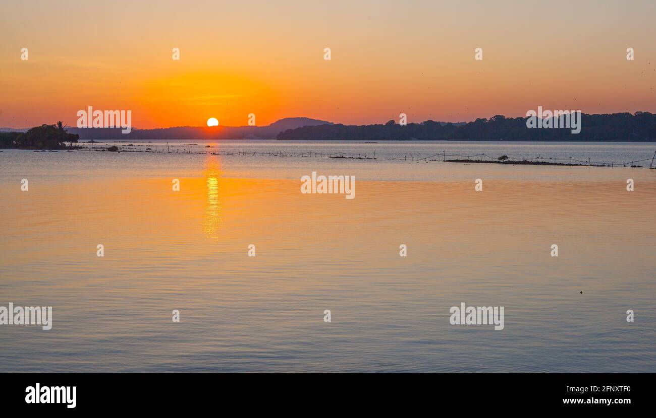 Sole che scende su un orizzonte lontano lasciando il cielo arancione e le acque turchesi blu, Trincomalee, Sri Lanka Foto Stock