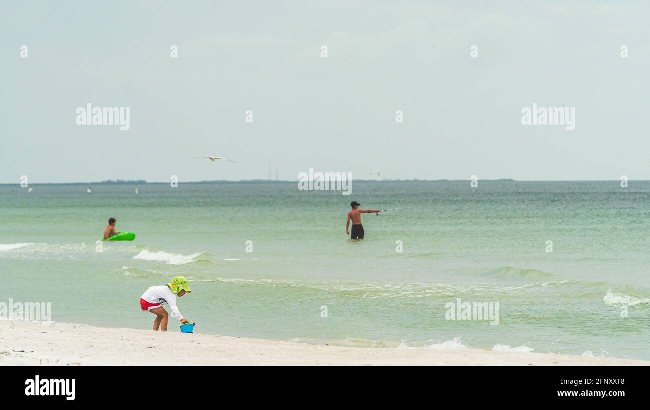 Il bambino piccolo nel cappello del floppy gioca nella sabbia lungo la riva di spiaggia Foto Stock