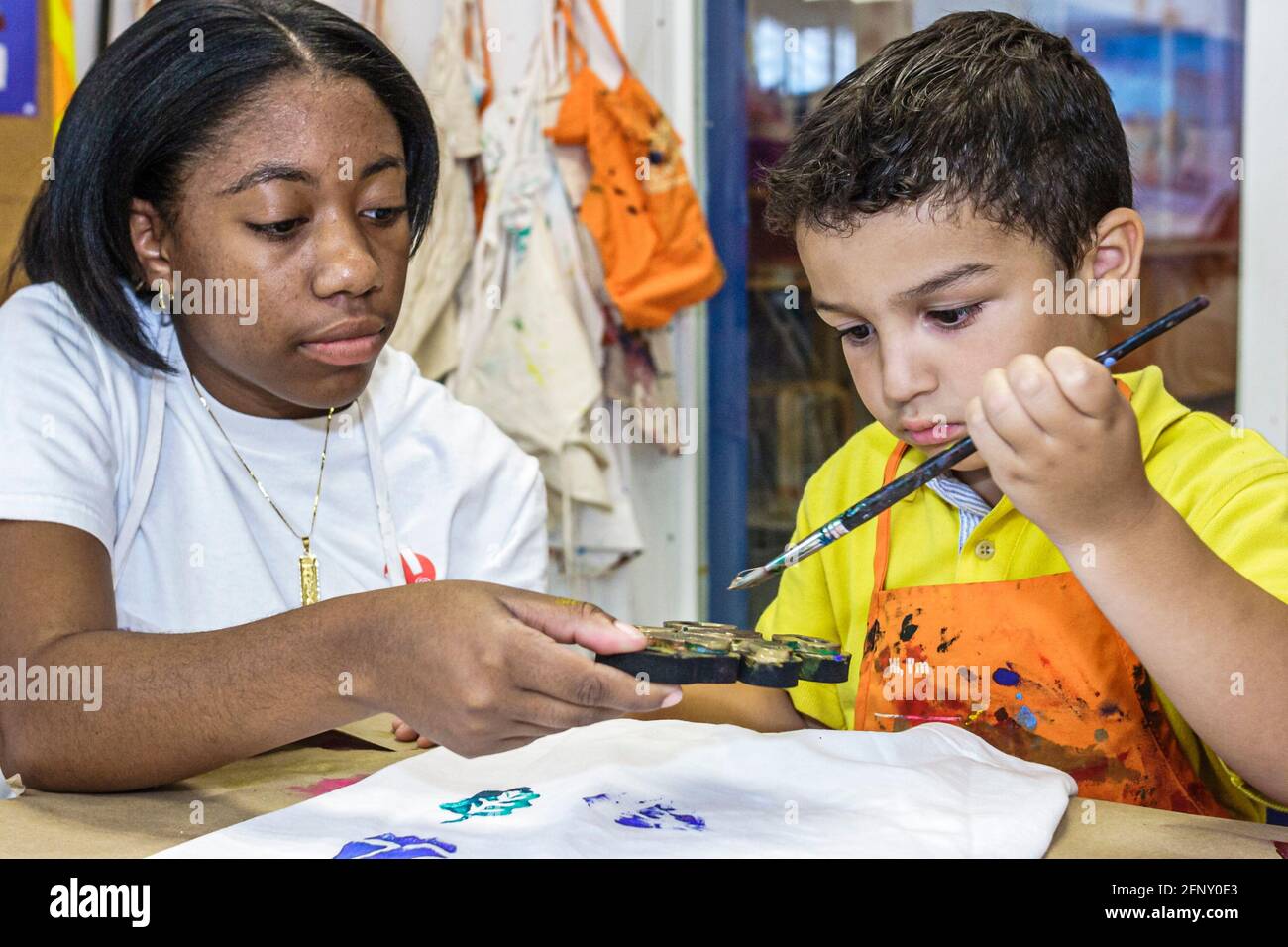 Miami Florida,laboratorio di decorazione tee-shirt del museo dei bambini,ragazzo ispanico bambino pittura ragazza nera femmina,adolescente adolescente studente volontario Foto Stock