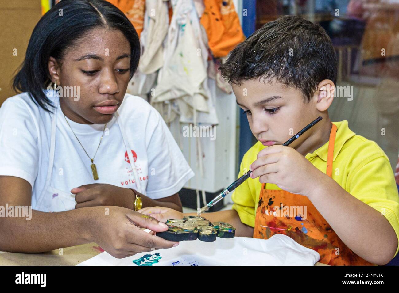 Miami Florida,laboratorio di decorazione tee-shirt del museo dei bambini,ragazzo ispanico bambino pittura ragazza nera femmina,adolescente adolescente studente volontario Foto Stock