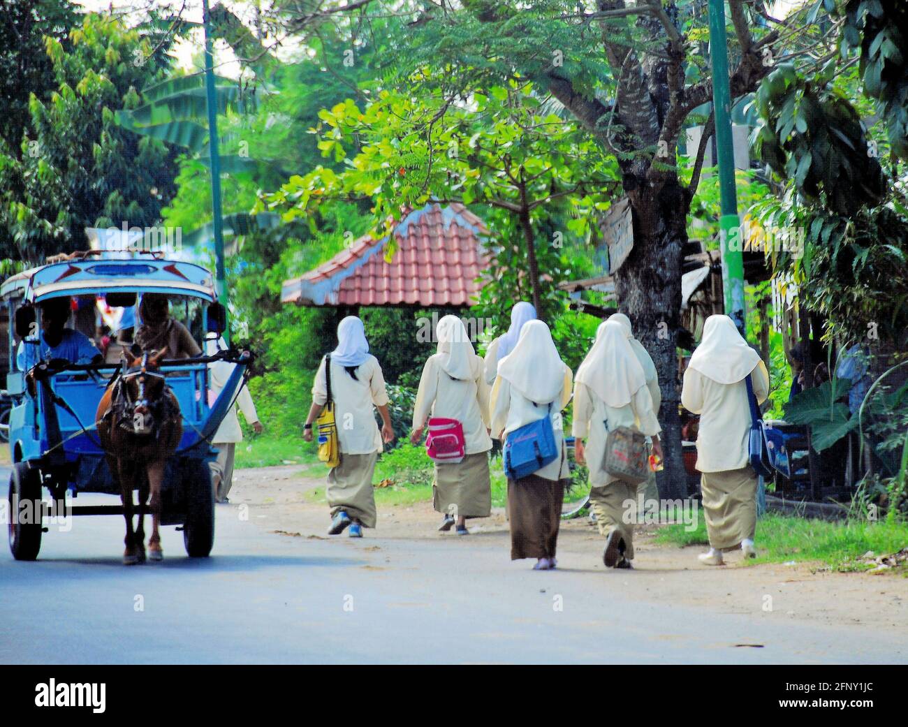Un gruppo di studentesse che vanno a scuola sul lato della strada mentre un carro trainato da cavalli si sta muovendo nel centro delle strade di Lombok, Indonesia. Foto Stock