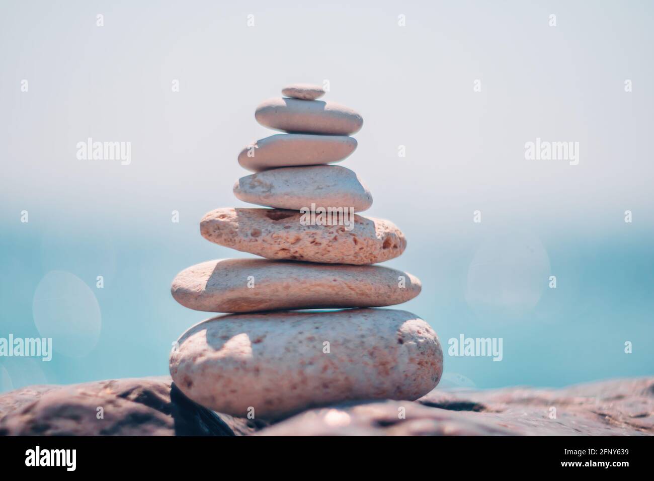 Equilibrata piramide di ciottoli sulla spiaggia in una giornata di sole. Abstract Sea bokeh sullo sfondo. Messa a fuoco selettiva. Pietre Zen sulla spiaggia di mare, meditazione Foto Stock