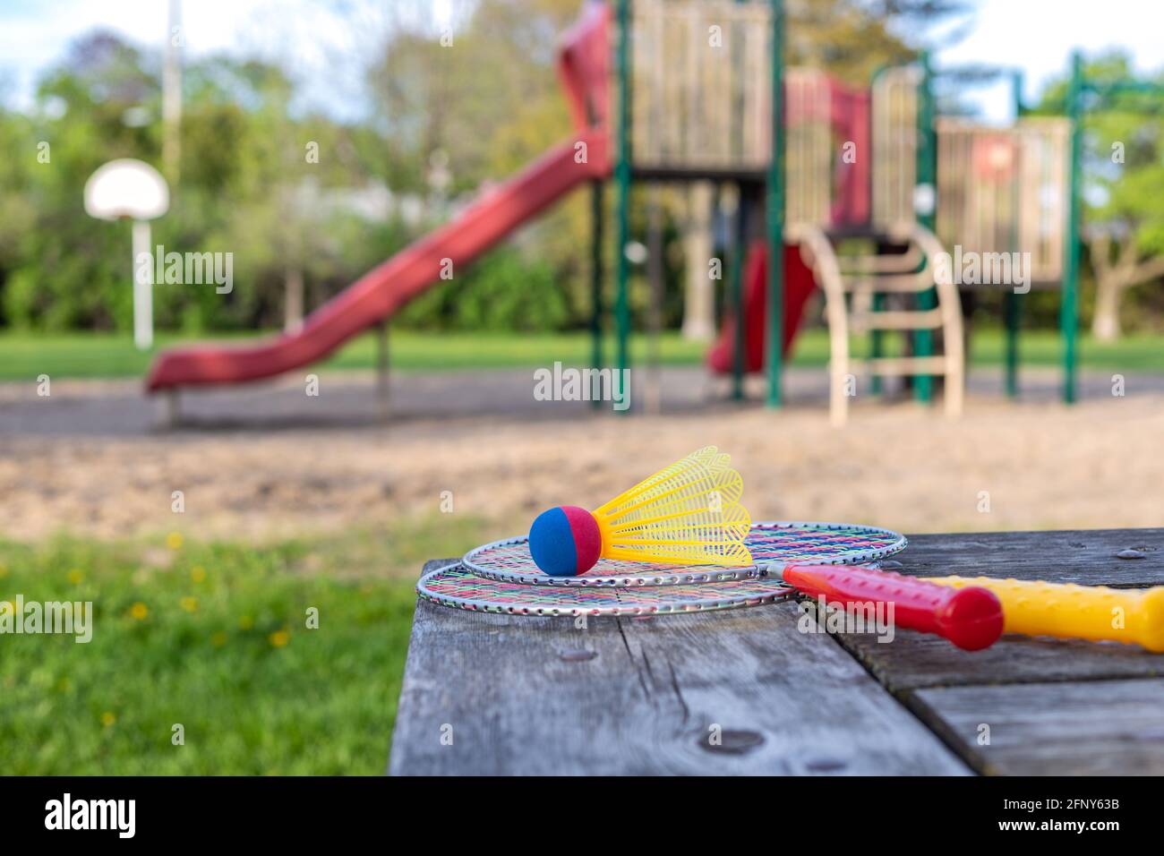 Racchette da gioco e shuttlecock di badminton su tavolo di legno e parco giochi per bambini nel backgroud nel parco in una giornata estiva soleggiata. Stile di vita attivo co Foto Stock