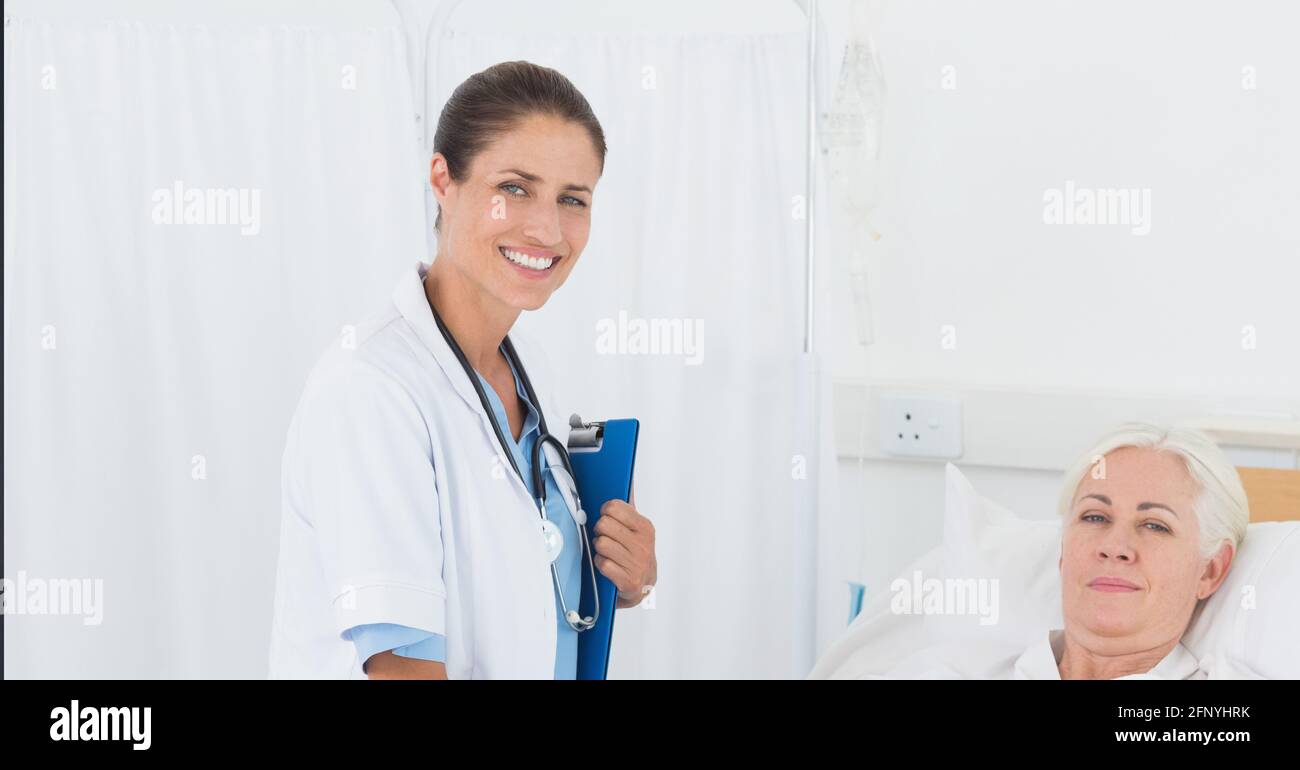 Ritratto di femmina caucasica dottore tenendo appunti sorridente mentre femmina paziente nel letto dell'ospedale Foto Stock