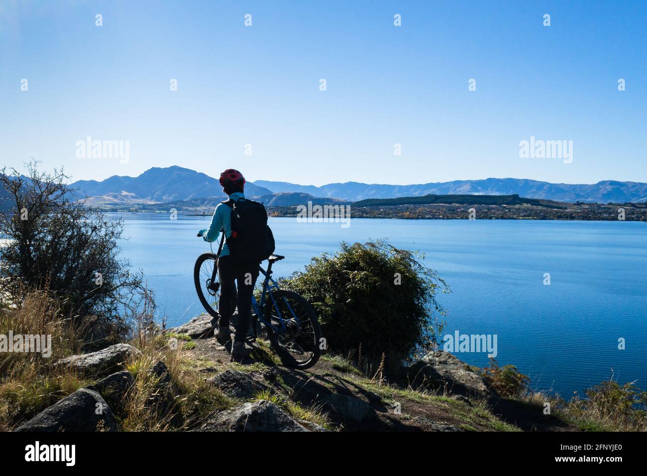 Una ciclista femminile in piedi con la sua bicicletta godendo la vista del Lago Wanaka, Isola del Sud Foto Stock