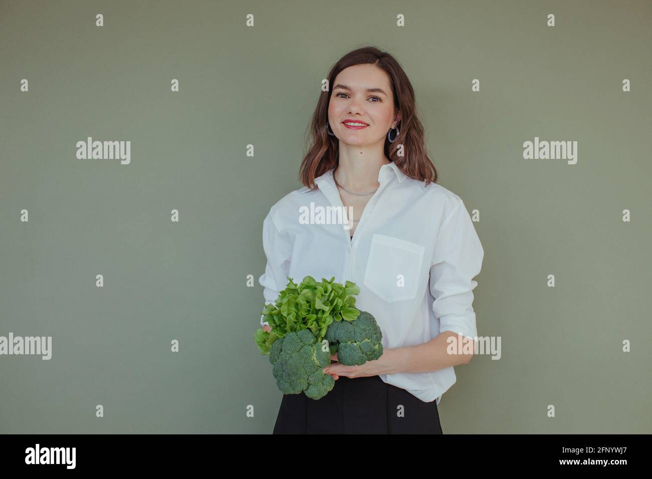 Ritratto di una bella donna sorridente che tiene freschi broccoli e. lattuga Foto Stock