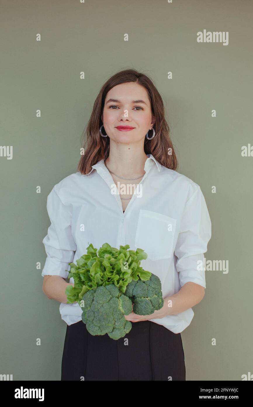 Ritratto di una bella donna sorridente che tiene freschi broccoli e. lattuga Foto Stock