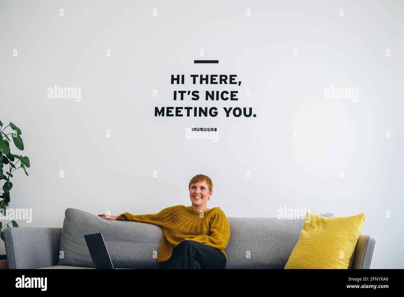 Donna d'affari sorridente sul divano nella lobby. Giovane donna professionista che guarda via e pensa nella lobby degli uffici. Foto Stock