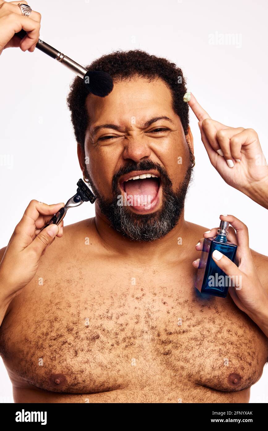 La barba per la cura di molte mani è un uomo. Mani di donne con spazzola per il trucco, rasoio, crema e bottiglia di profumo che cura un uomo eccitato. Foto Stock