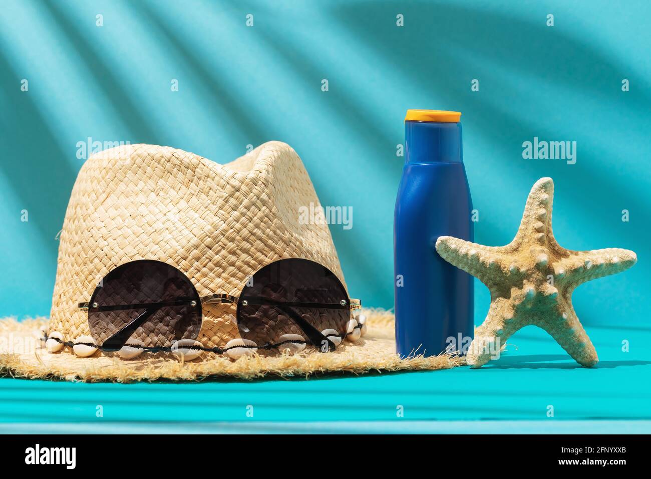 Cappello di paglia da donna, occhiali da sole, crema solare e stelle marine su sfondo colorato. Foto Stock