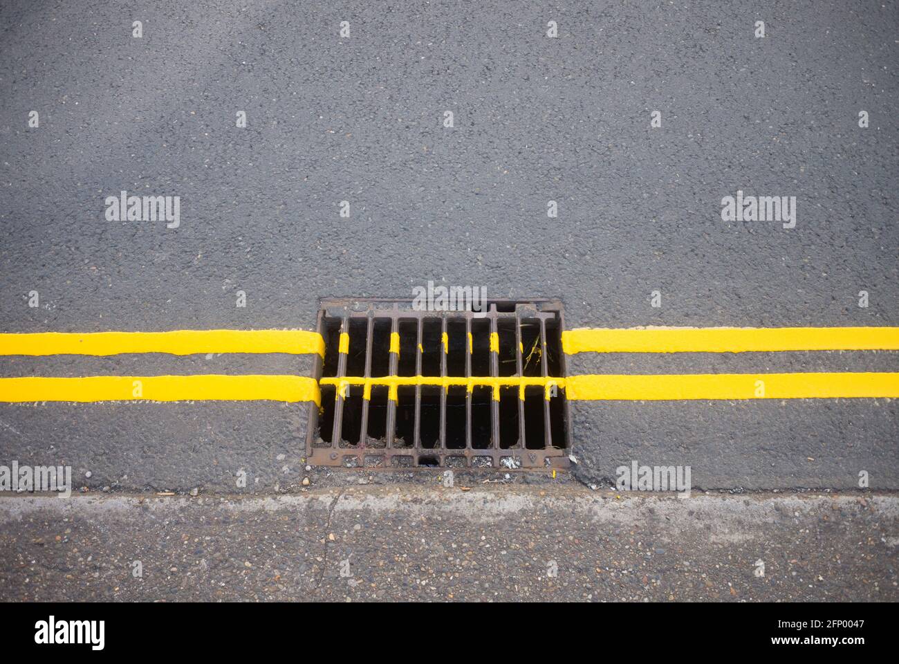 Due linee gialle che vanno oltre uno scarico nella strada Foto Stock