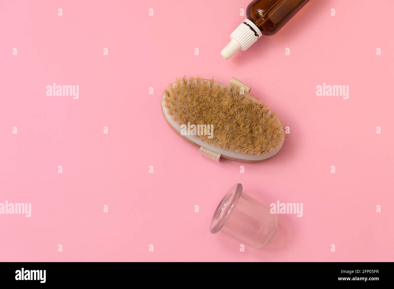 Composizione piatta con kit massaggio: Spazzola a secco, massaggiatore a ventosa, bottiglia d'olio su fondo rosa morbido con spazio per il testo Foto Stock
