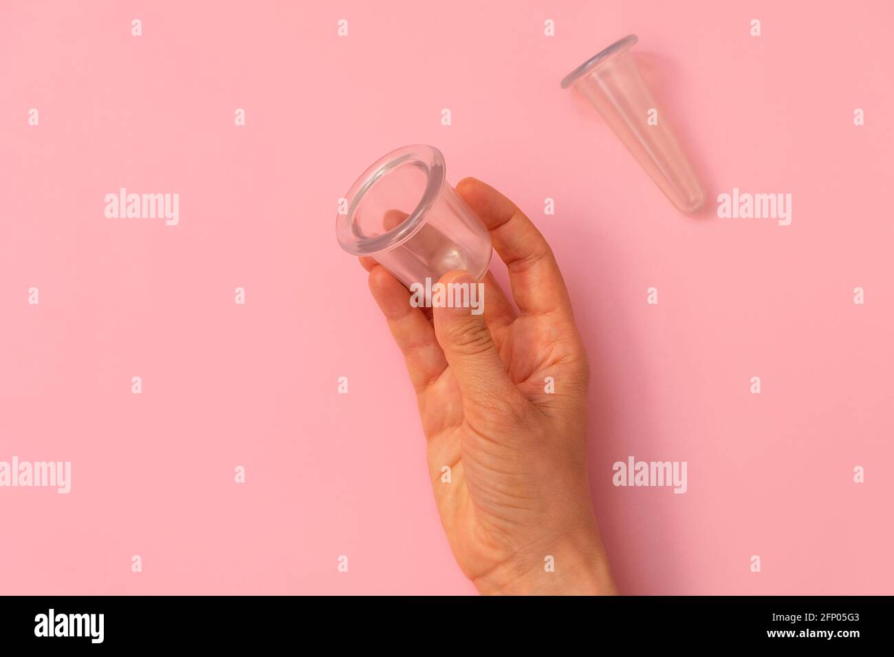 Vista dall'alto della mano della donna che tiene una tazza sottovuoto in silicone per il massaggio di imbutitura su sfondo rosa pastello con spazio per la copia Foto Stock