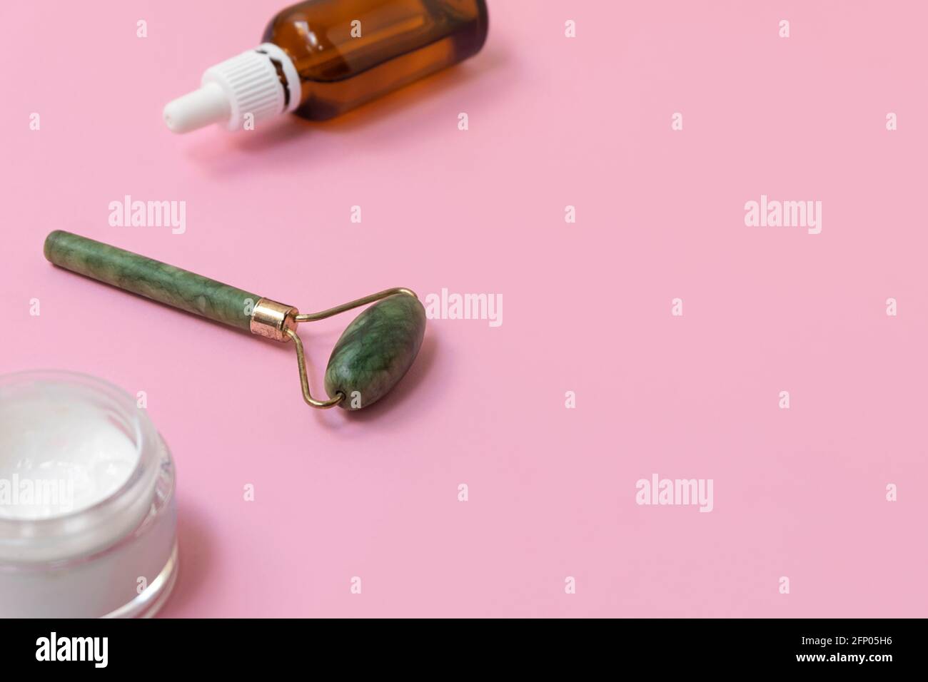 Rullo per il viso Jade per la terapia del massaggio facciale di bellezza. Strumenti di bellezza su sfondo rosa pastello con spazio di copia Foto Stock