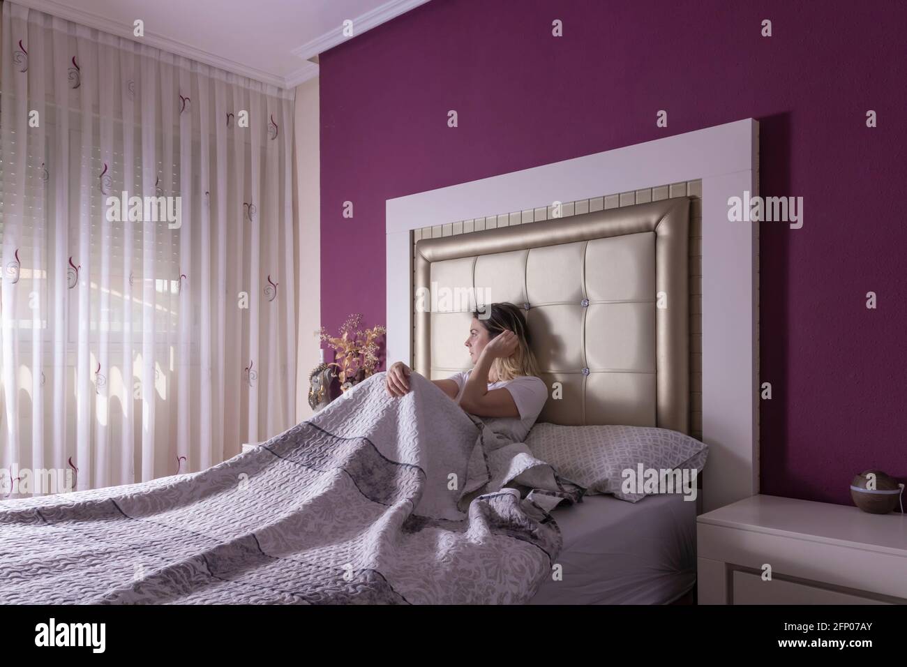 giovane bella donna seduta in letto sotto le coperte, appena svegliata Foto Stock