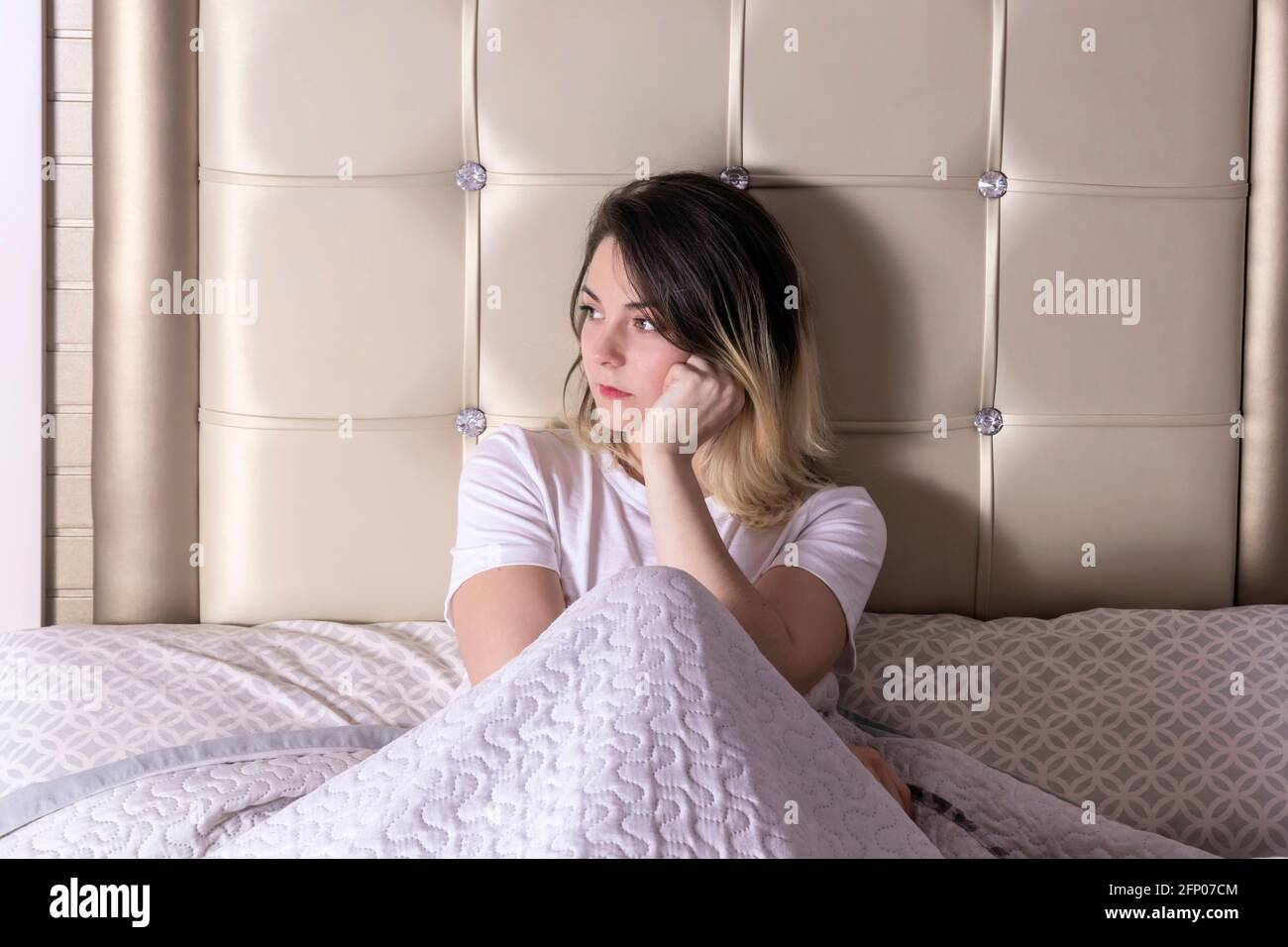 giovane bella donna seduta in letto sotto le coperte, appena svegliata Foto Stock