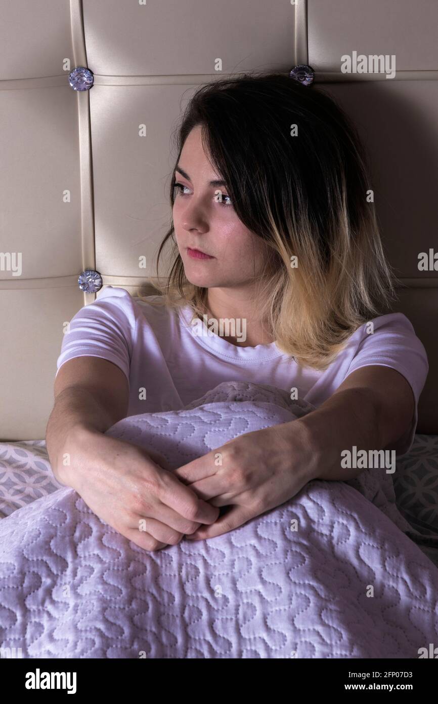 giovane bella donna seduta in letto sotto le coperte, appena svegliata Foto Stock
