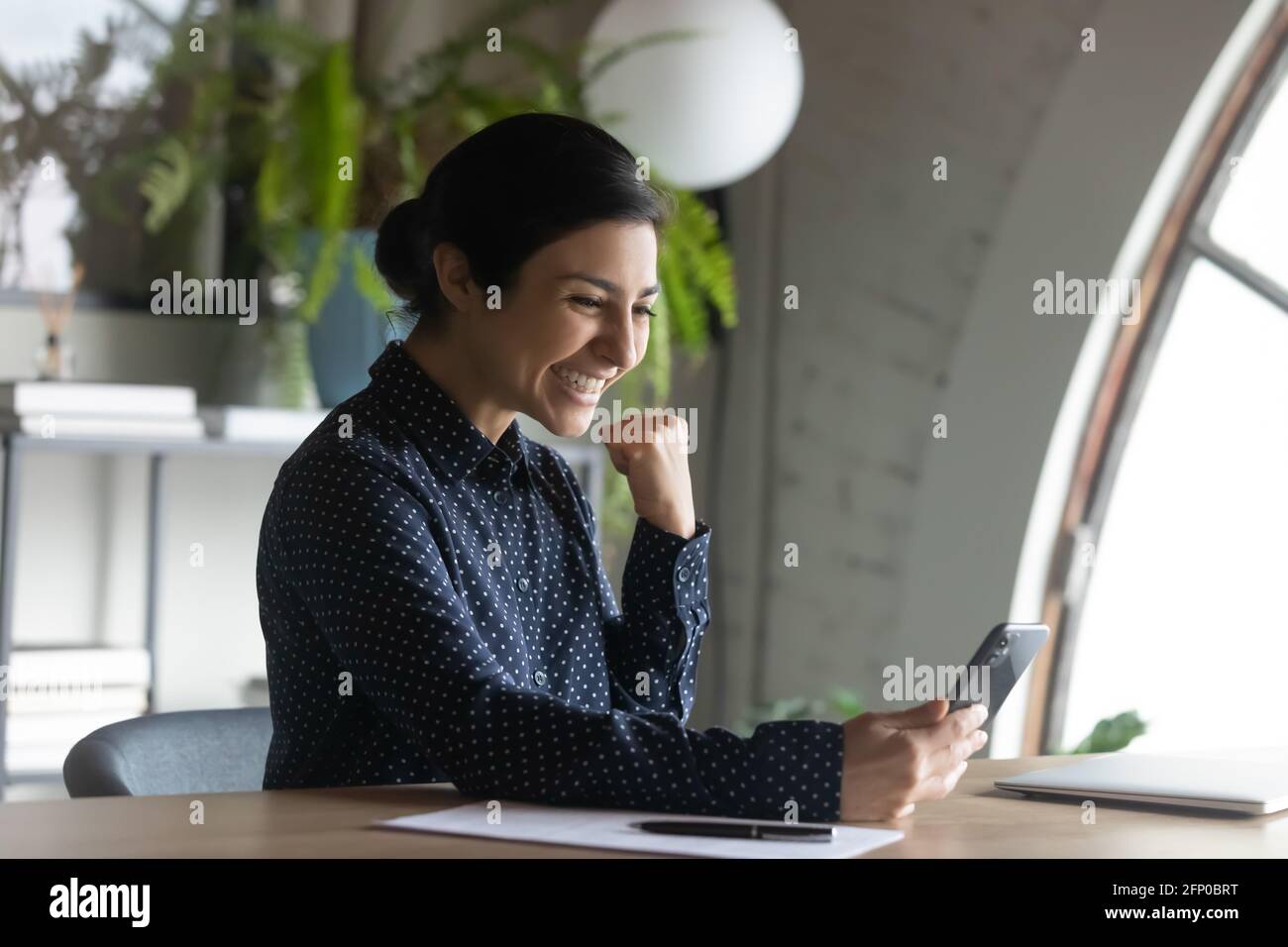 La donna etnica eccitata si sente euforica con le notizie sulle cellule Foto Stock