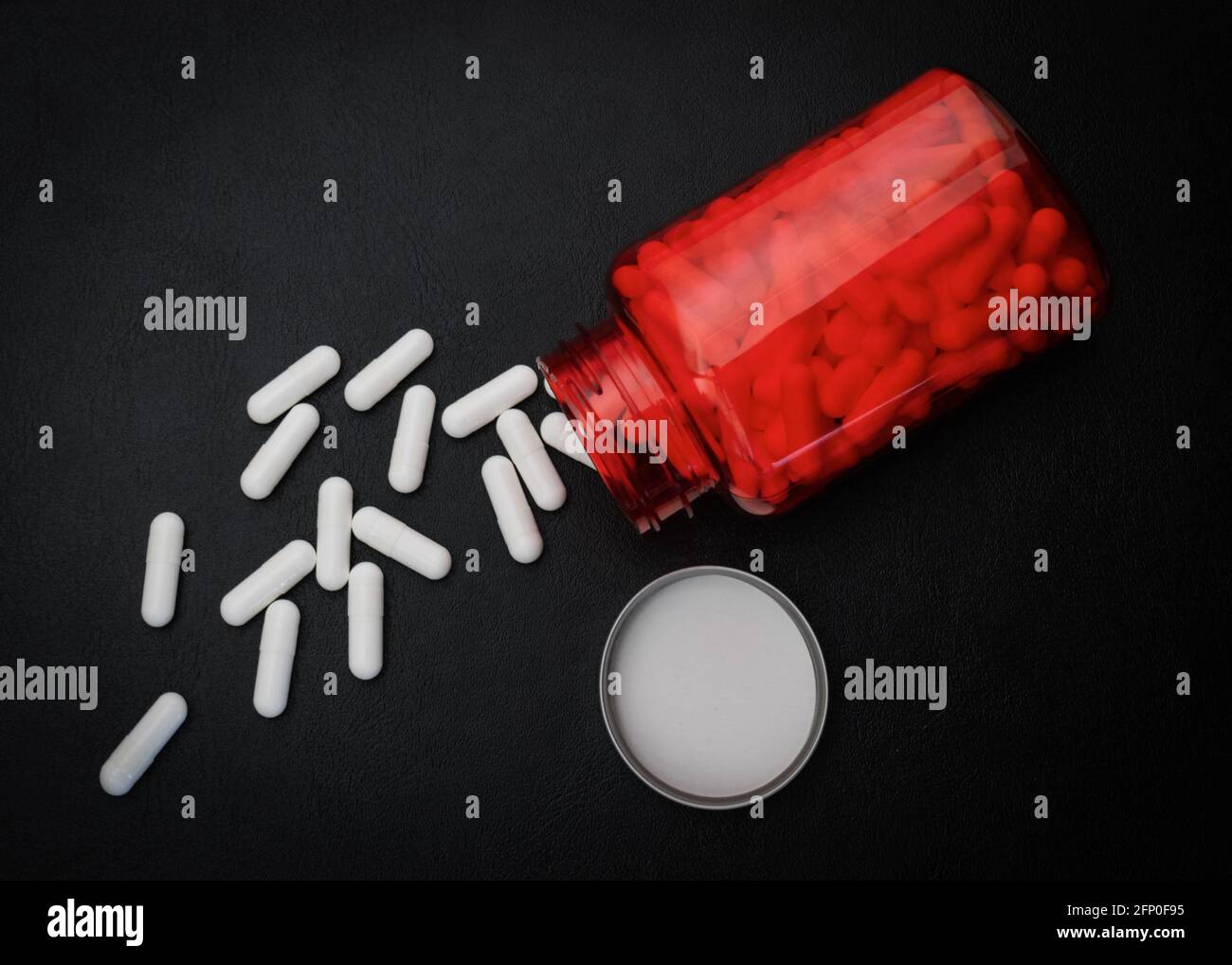Compresse di medicina bianca o vitamine in un flacone rosso su uno sfondo nero Foto Stock