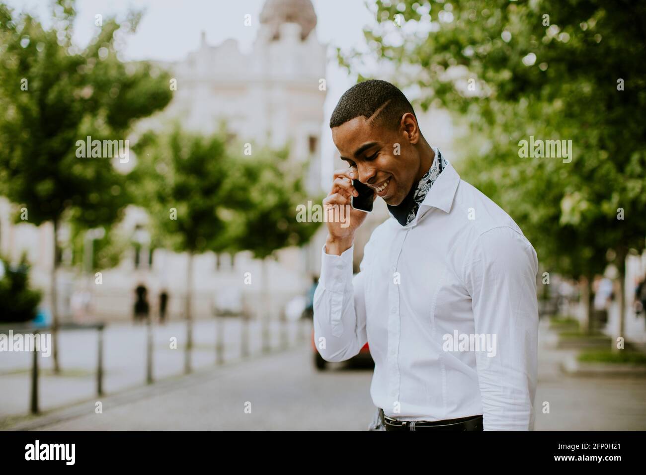 Bel giovane uomo d'affari afro-americano che usa un telefono cellulare mentre attesa di un taxi in attesa di un taxi su una strada Foto Stock