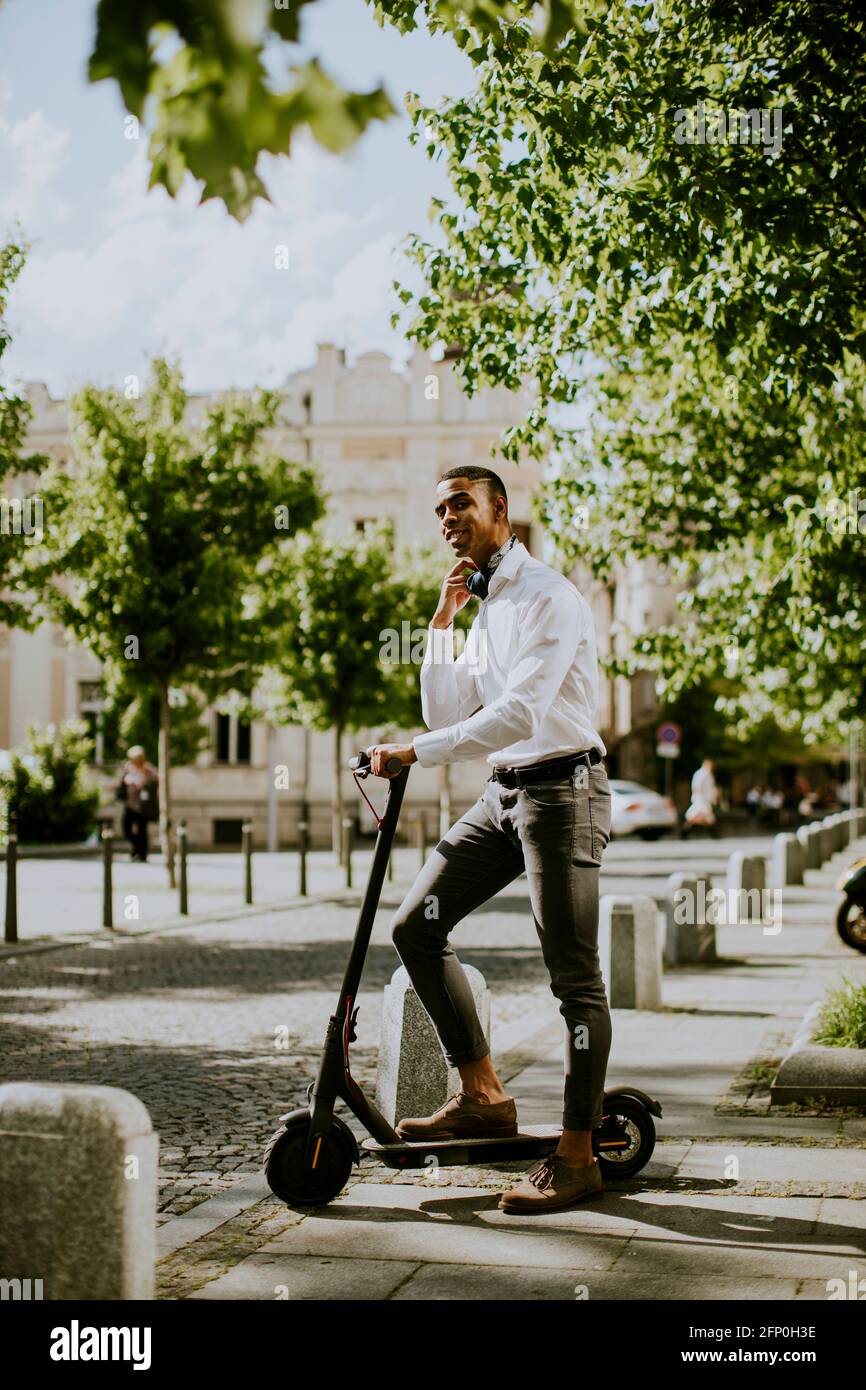 Bel giovane afroamericano con scooter elettrico su una strada Foto Stock