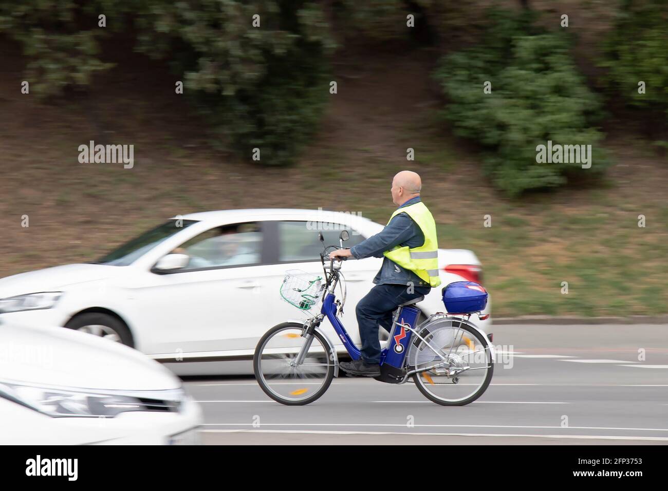 Belgrado, Serbia - 14 maggio 2021: Un uomo anziano che indossa un giubbotto fluorescente a bordo di una bicicletta elettrica nel traffico cittadino di strada vicino al parco Foto Stock