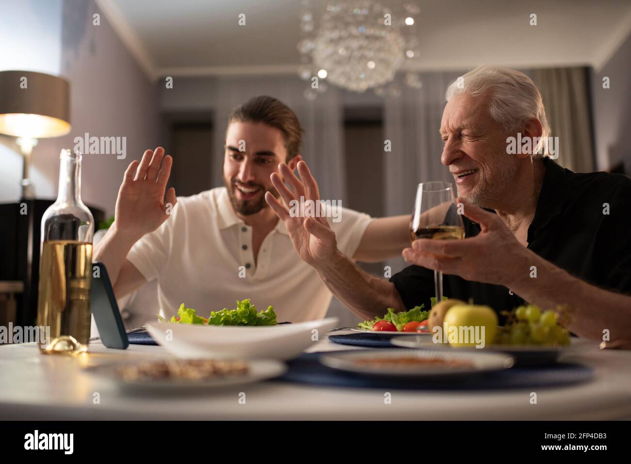 Nonno e nipote salutano un parente online durante la cena Foto Stock