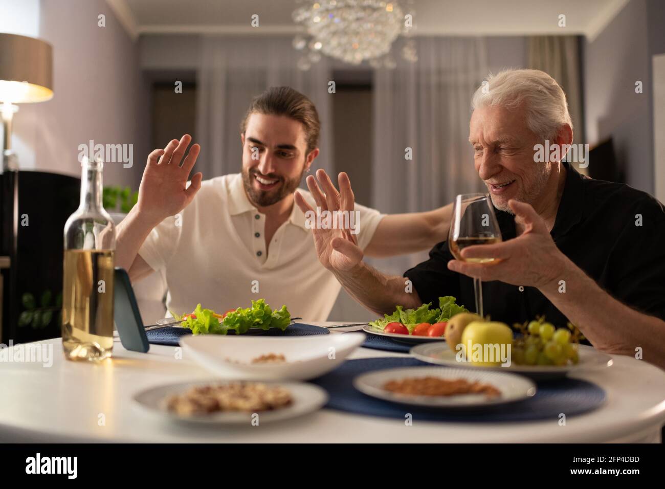Nonno e nipote che parlano con un parente online durante la cena Foto Stock