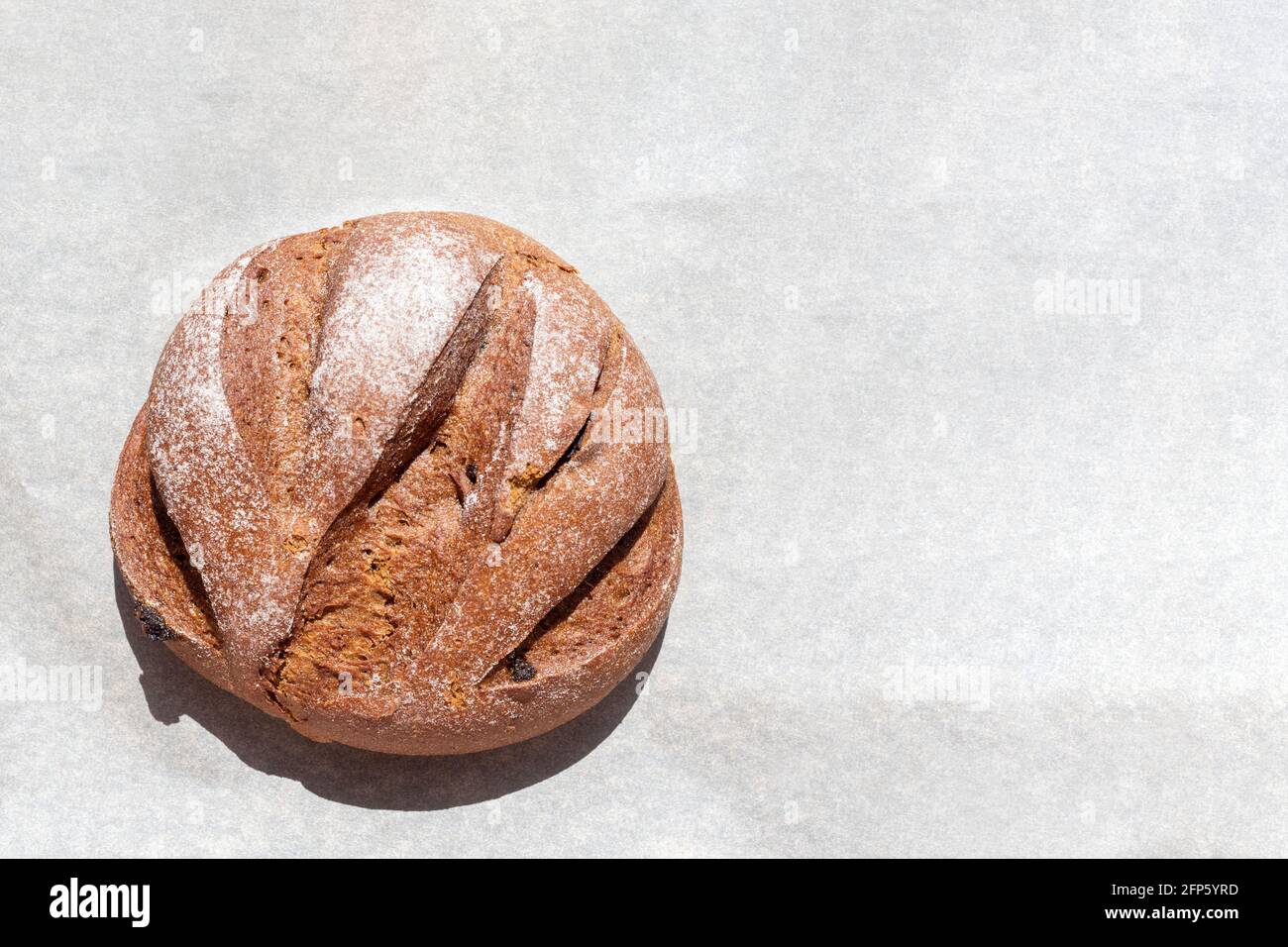 Pane all'uvetta rotondo di segale appena sfornato su carta da forno, vista dall'alto, spazio per la copia. Concetto di cibo sano, i benefici del pane Foto Stock