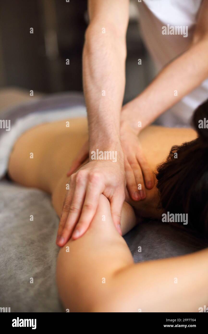 Master senza volto che dà massaggio di muscoli della schiena e delle spalle a. donna anonima sdraiata sul tavolo nel salone termale Foto Stock