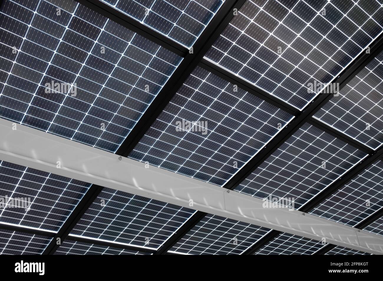 Pannelli solari installati su travi in acciaio per coprire un parcheggio, visto dal basso. Energia sostenibile e ombra allo stesso tempo Foto Stock