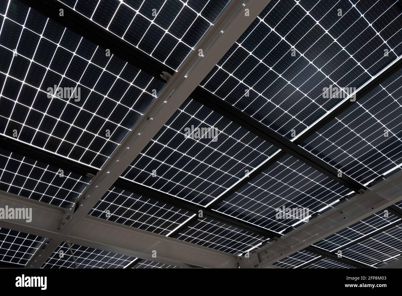 Pannelli solari installati su travi in acciaio per coprire un parcheggio, visto dal basso. Energia sostenibile e ombra allo stesso tempo Foto Stock