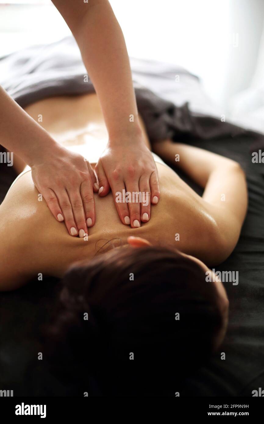 Master senza volto che dà massaggio di muscoli della schiena e delle spalle a. donna anonima sdraiata sul tavolo nel salone termale Foto Stock