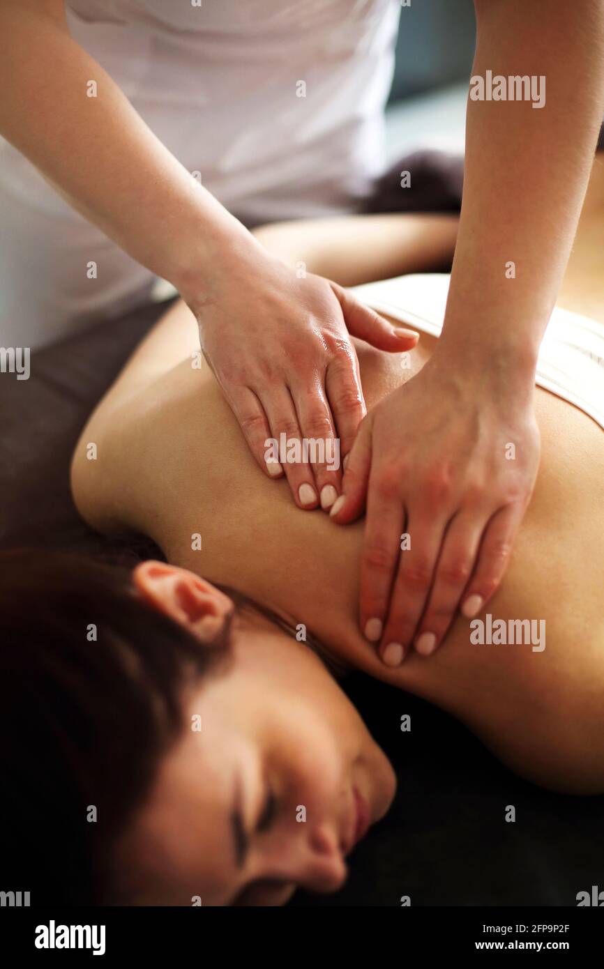 Master senza volto che dà massaggio di muscoli della schiena e delle spalle a. donna anonima sdraiata sul tavolo nel salone termale Foto Stock
