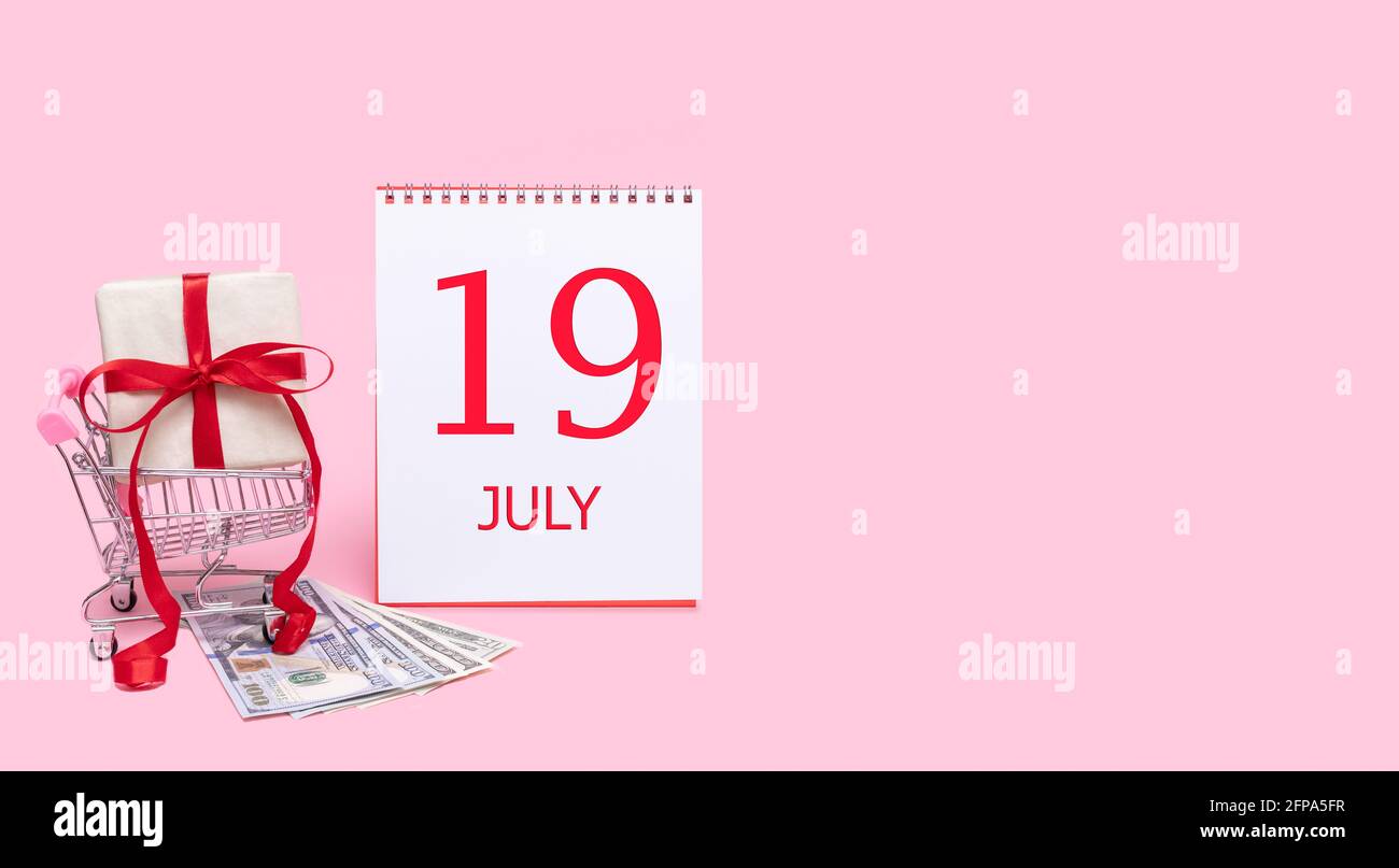 19 luglio. Una confezione regalo in un carrello, dollari e un calendario con la data del 19 luglio su sfondo rosa. Mese estivo, giorno del yea Foto Stock