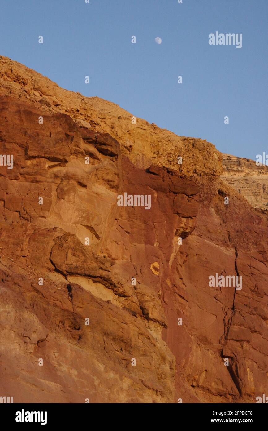 Scogliera di arenaria rossa ha il ferro in essa, è un muro del piccolo Makhtesh formato da erosione nel deserto di Negev, la luna del pomeriggio è sopra Foto Stock