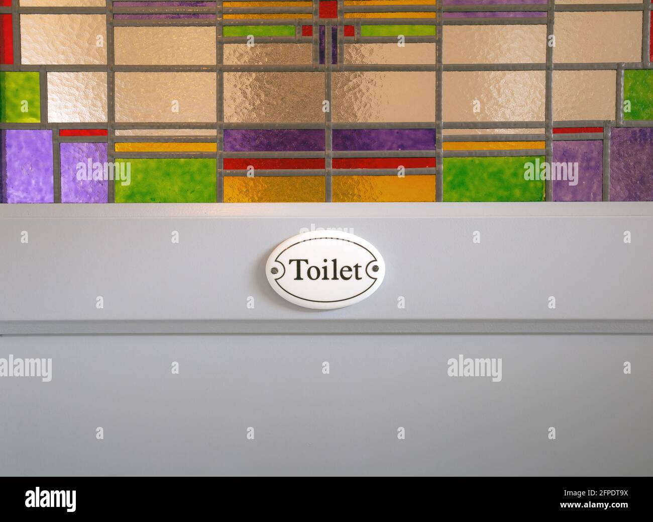 Porta in legno grigio con testo dei segni del gabinetto e colorate vetrate nell'edificio, motivo sfondo guardaroba dal design moderno Foto Stock