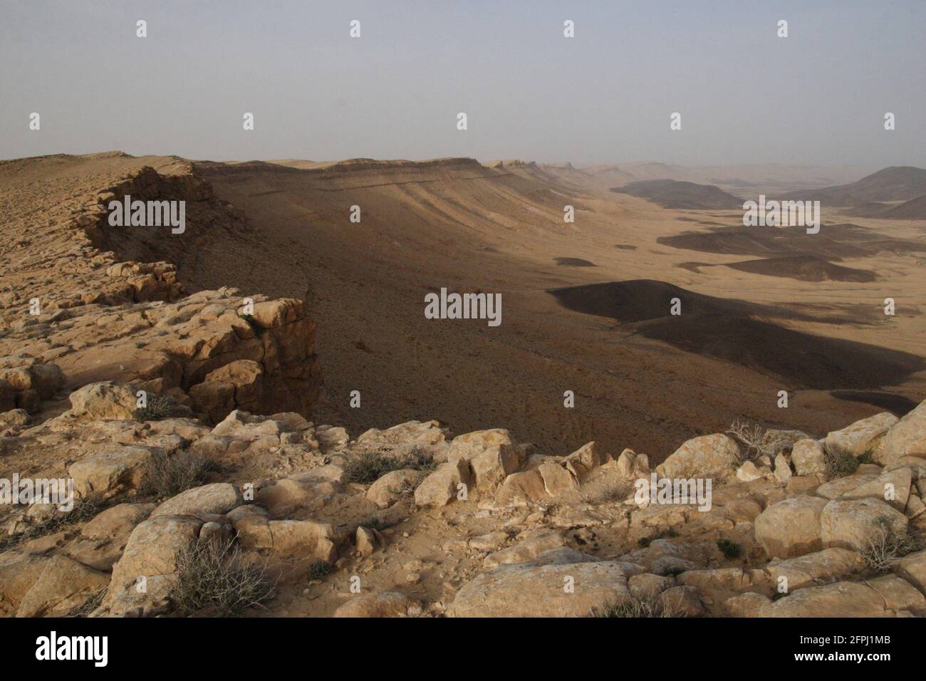 Makhtesh Ramon, un enorme cratere creato dall'erosione in tempi geologici antichi come visto dal bordo occidentale, le colline nere sono depositi di rocce basaltiche. Foto Stock