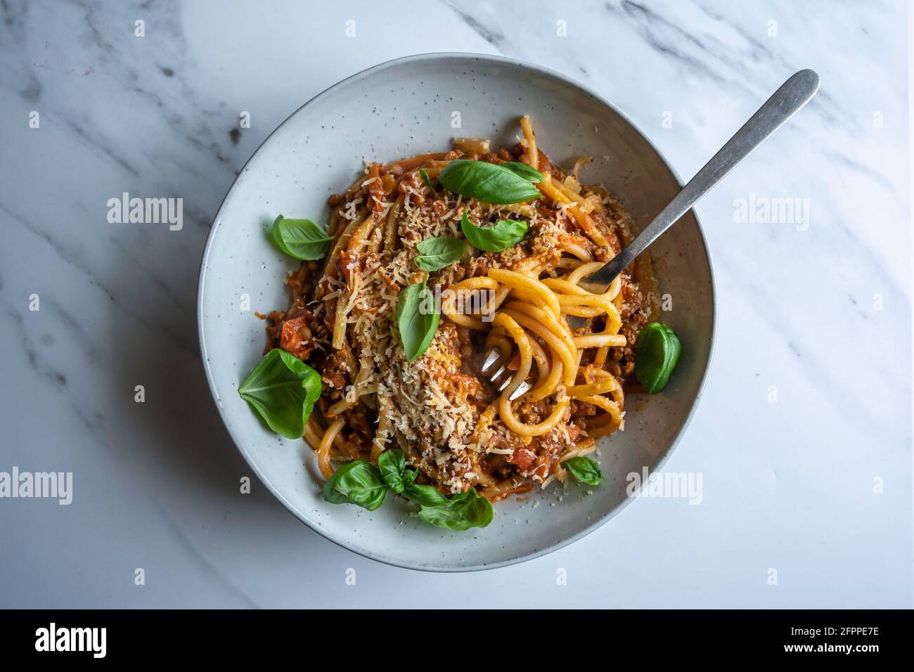 Pasta di lenticchie vegane, bucatini con salsa di lenticchie di pomodoro fresca fatta in casa, basilico e parmigiano su fondo di cemento bianco con spazio per la copia Foto Stock