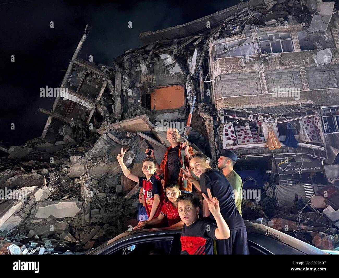 La gente si avvicina alle macerie di un edificio danneggiato mentre i palestinesi celebrano nelle strade dopo un cessate il fuoco, a Gaza City 21 maggio 2021. REUTERS/Mohammed Salem Foto Stock