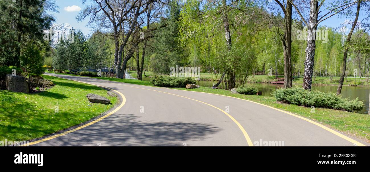 Strada attraverso il parco. Sentiero asfaltato per pedoni e ciclisti attraverso una splendida vegetazione e un lago nel parco Foto Stock