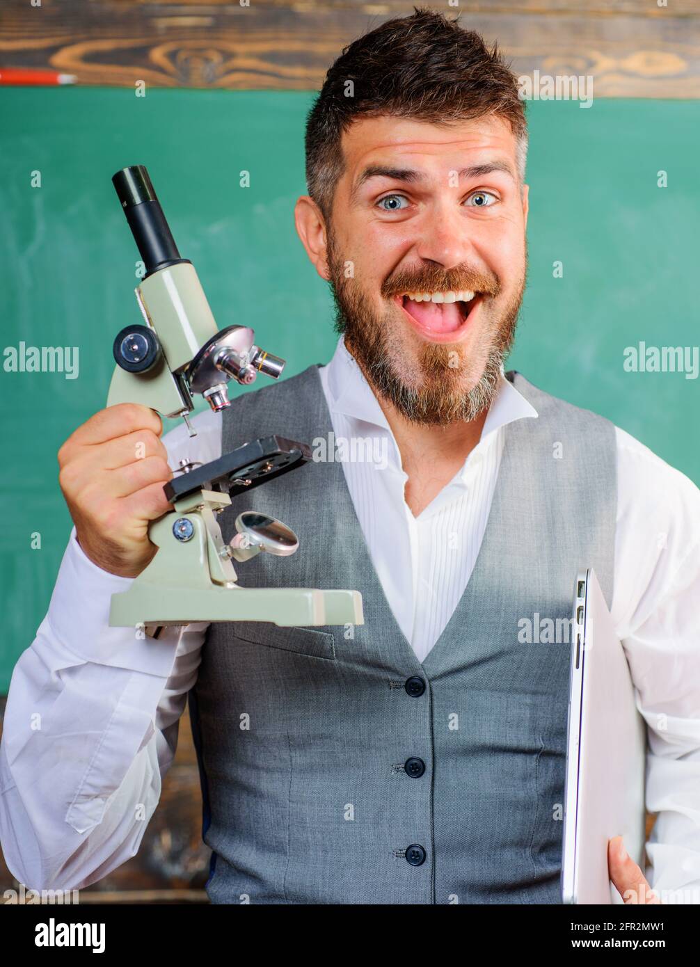 Concetto di biologia o chimica. Felice insegnante con computer e microscopio. Insegnante entusiasta in classe. Foto Stock