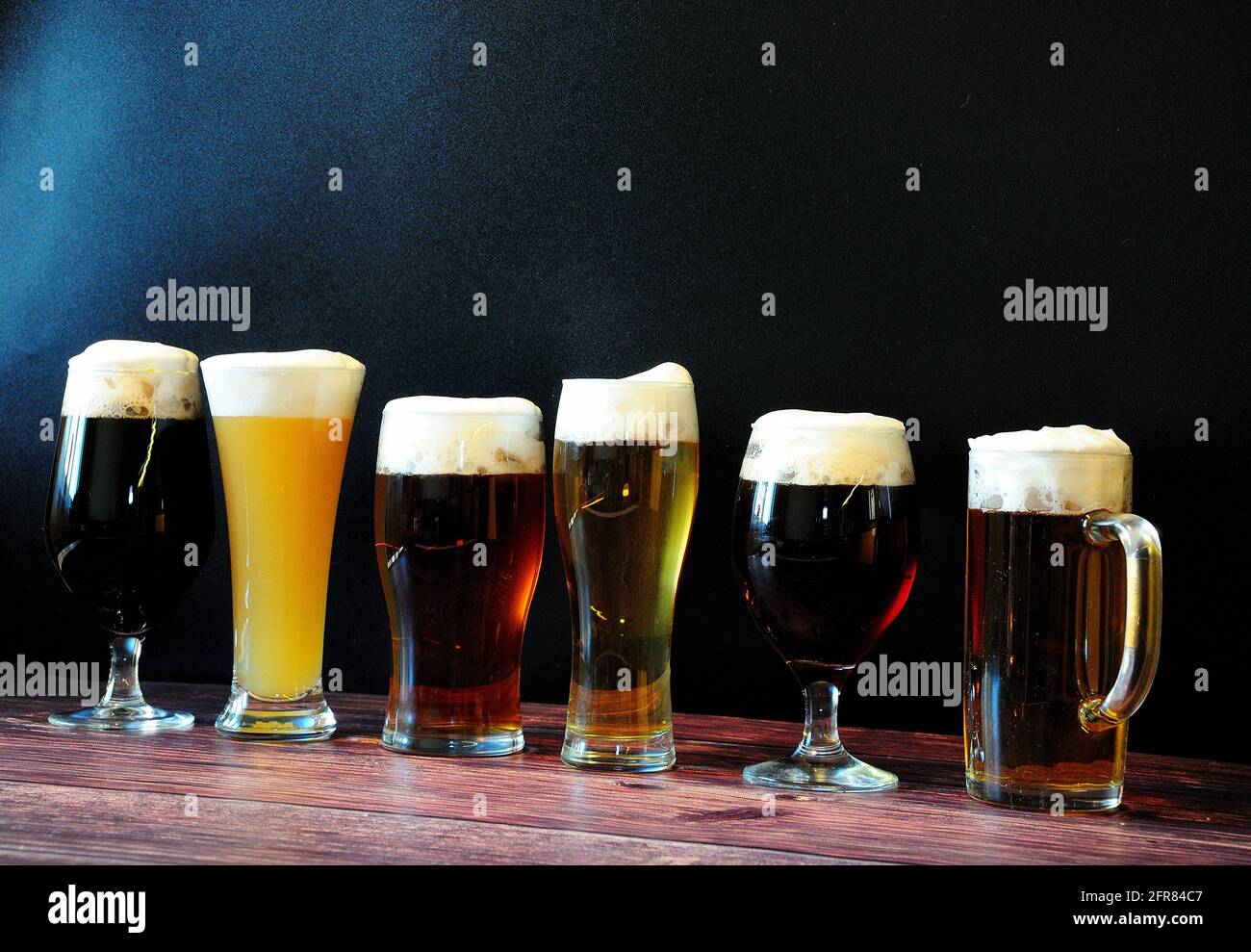 Sei bicchieri di diverse birre sono su un tavolo di legno contro una parete nera. Primo piano. Foto Stock